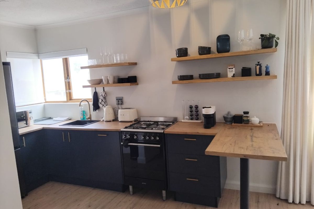Modern kitchen featuring dark cabinetry, wooden countertops, floating shelves, a gas stove, and an integrated breakfast bar area.