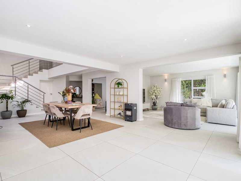 Spacious open-plan living and dining area featuring large format floor tiles, recessed lighting, and a modern staircase with a stainless steel balustrade.