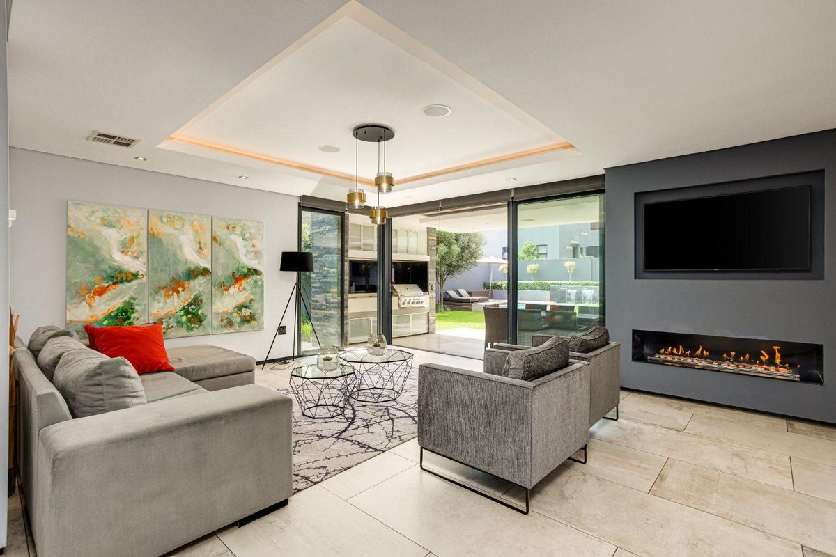 Modern open-plan living area featuring a built-in fireplace, recessed tray ceiling with ambient lighting, and large sliding glass doors opening to the patio.
