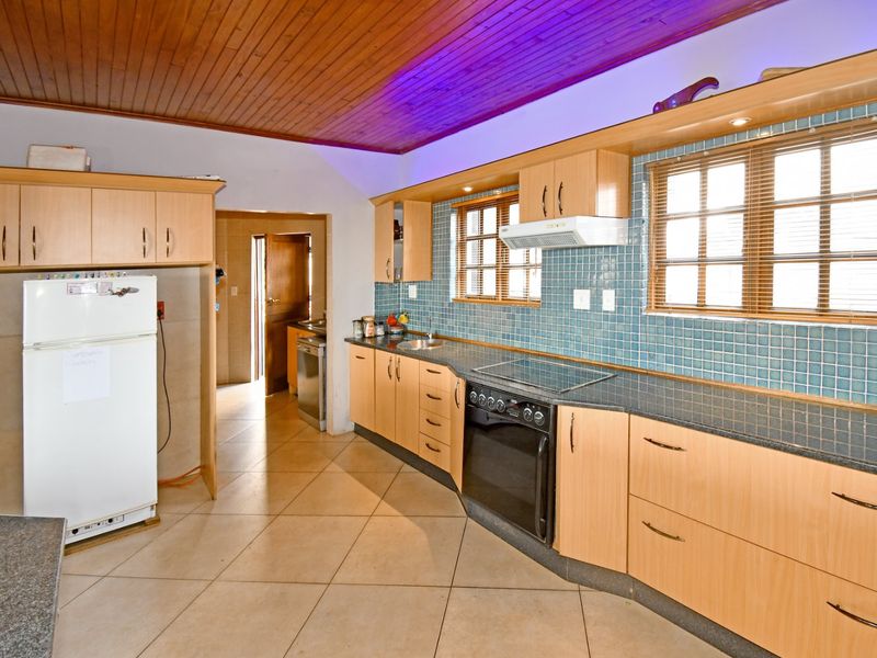 A functional kitchen featuring light wood cabinetry, dark countertops, a tiled backsplash, and a distinctive timber ceiling with integrated lighting.