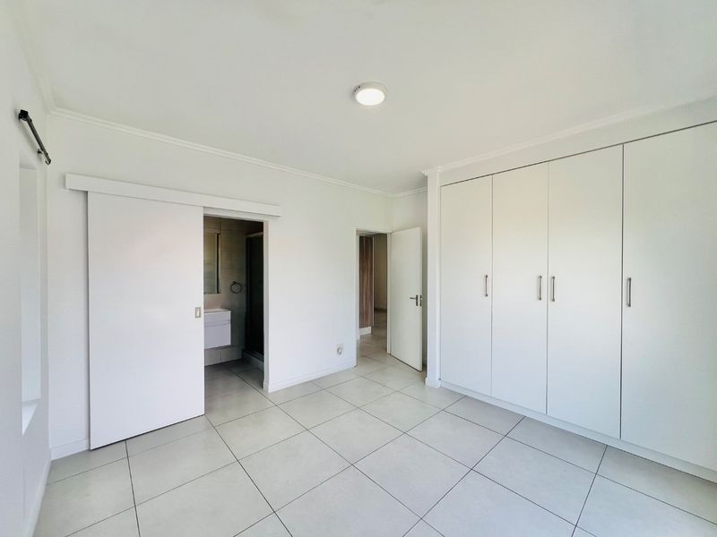 A bright, empty bedroom featuring neutral tiled flooring, ample built-in cupboard space, and direct access to an en-suite bathroom.