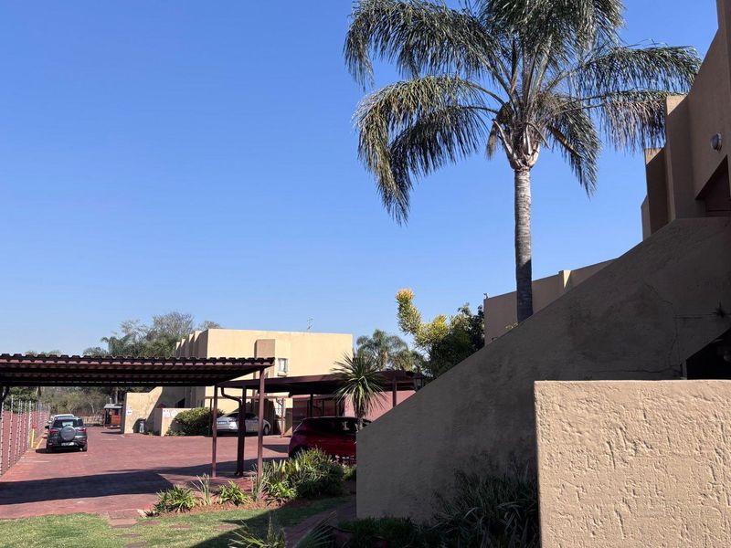 Exterior view of the apartment complex featuring a paved driveway, covered parking carports, and established landscaping.