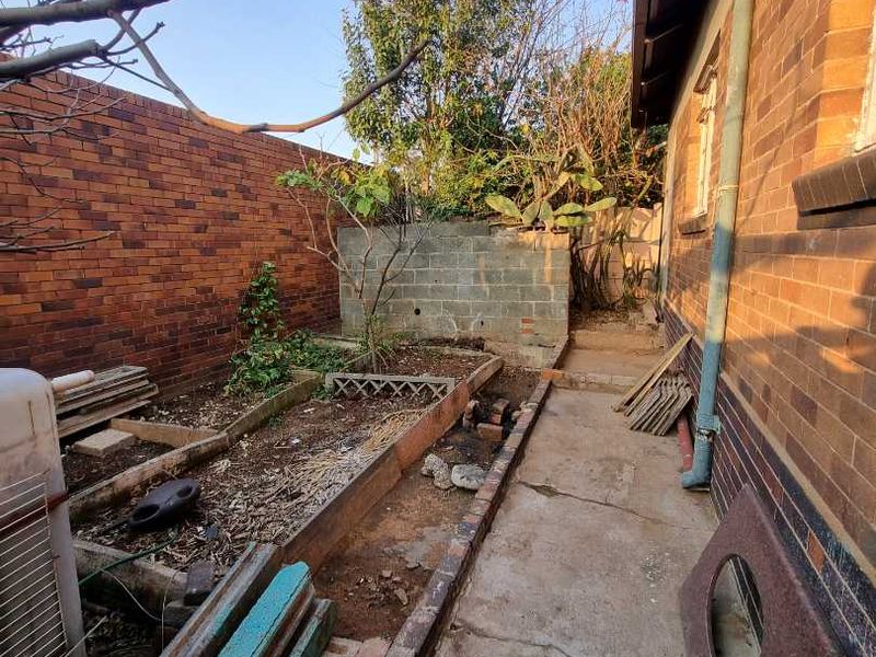 A rear exterior area featuring a concrete pathway, brick boundary walls, and raised garden beds in need of maintenance and landscaping.