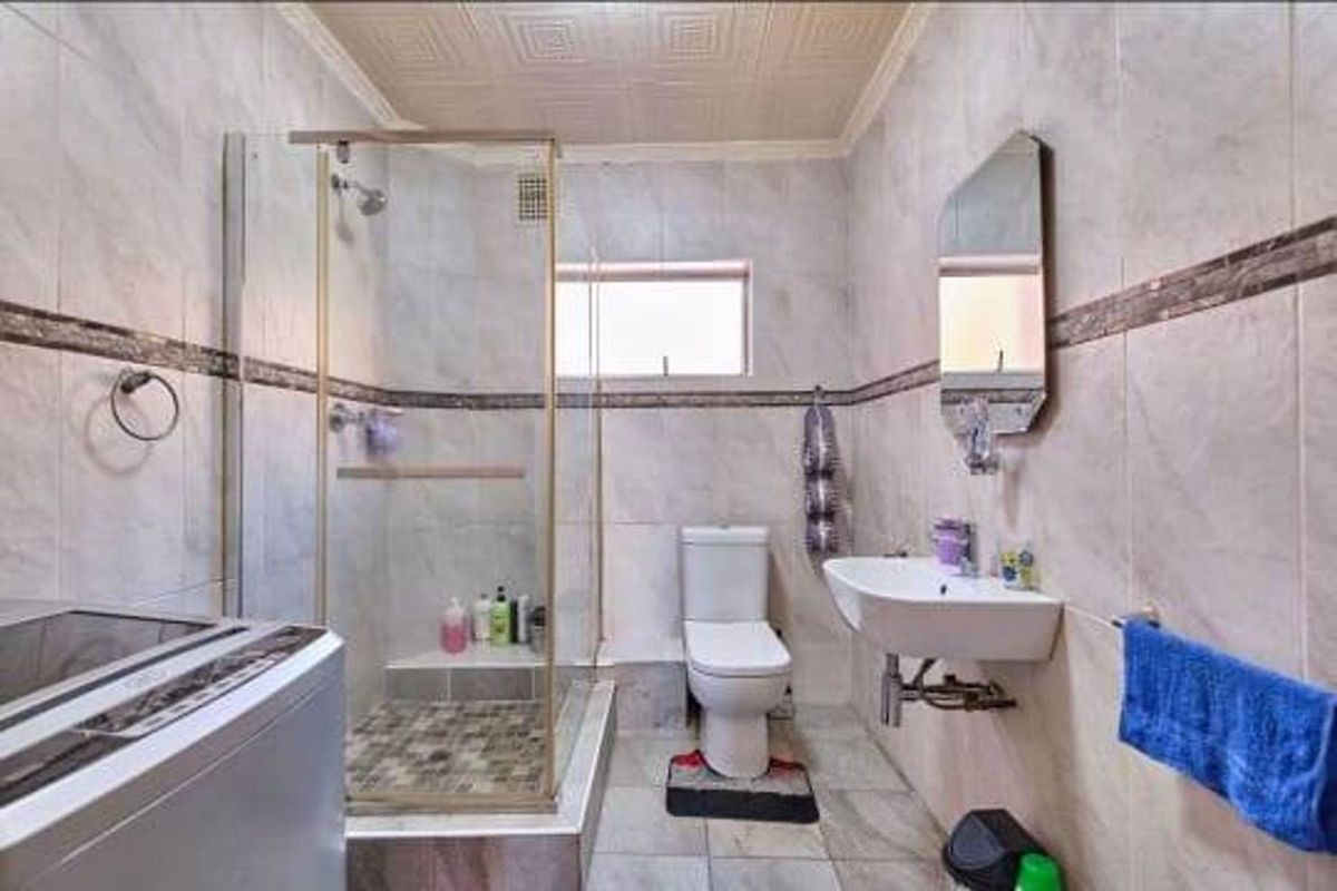 A functional bathroom featuring a glass-enclosed shower, wall-mounted basin, and toilet, with tiled walls and flooring throughout.