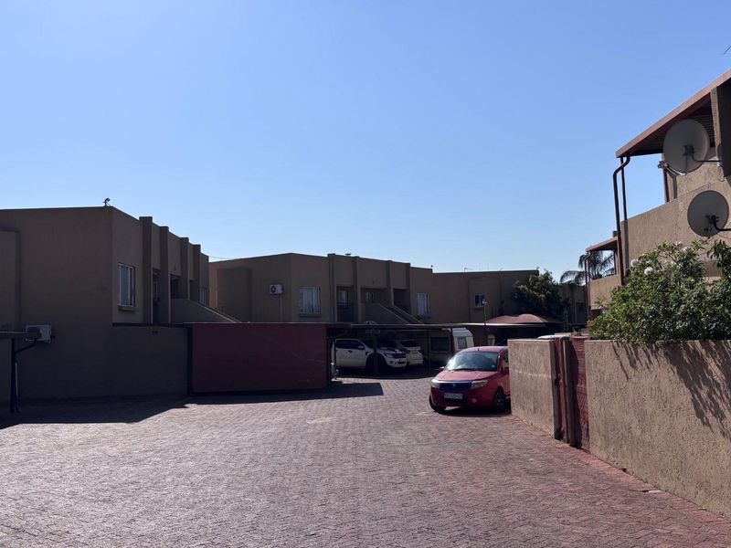 Exterior view of the apartment complex featuring a paved driveway, covered parking bays, and boundary walls.