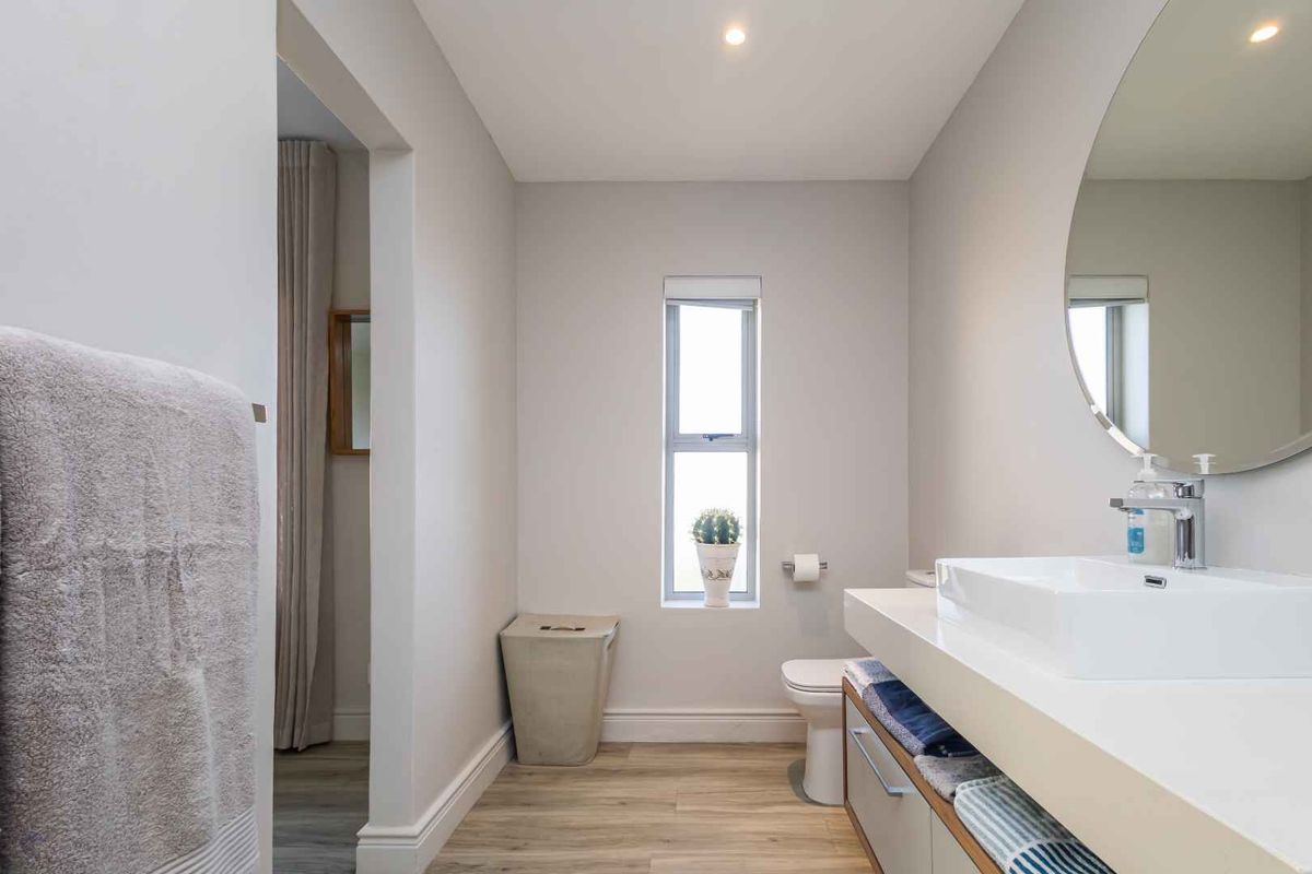 A modern, well-maintained bathroom featuring a sleek vanity with a vessel sink, a round wall-mounted mirror, and wood-look flooring.