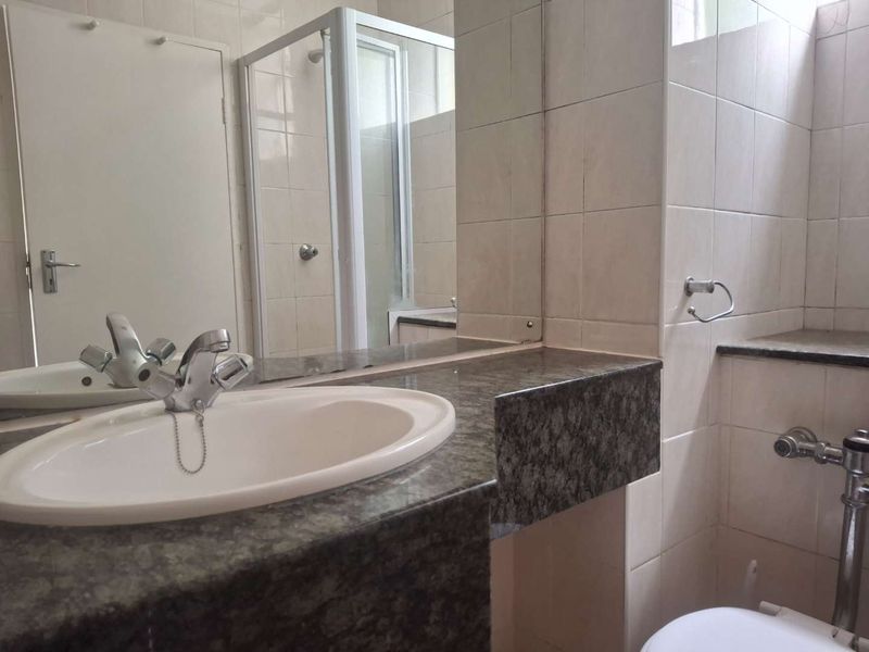 A functional bathroom featuring a granite-topped vanity, a shower enclosure, and neutral wall tiling, offering a clean and practical space.