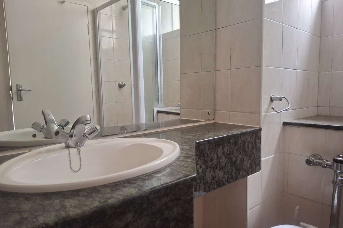 A functional bathroom featuring a granite-topped vanity, a shower enclosure, and neutral wall tiling, offering a clean and practical space.