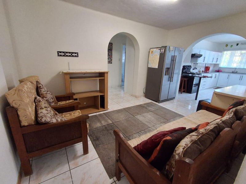 Open plan living area featuring tiled floors and an arched entryway leading to a functional kitchen with white cabinetry.