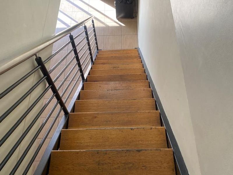A downward view of a timber staircase featuring a metal balustrade, leading to a tiled lower level living area.