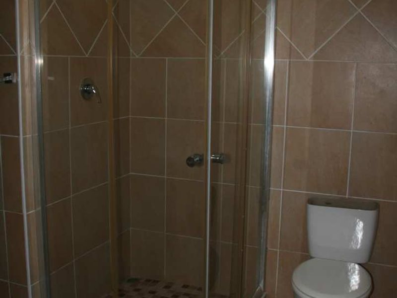 A functional bathroom featuring a corner shower enclosure with glass doors and a standard toilet, finished with neutral ceramic wall and floor tiling.