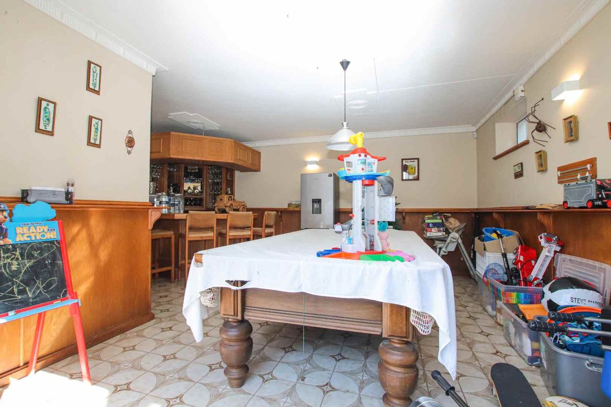 A spacious entertainment room featuring a built-in wooden bar, tiled flooring, and decorative crown molding, suitable for a games or recreation area.