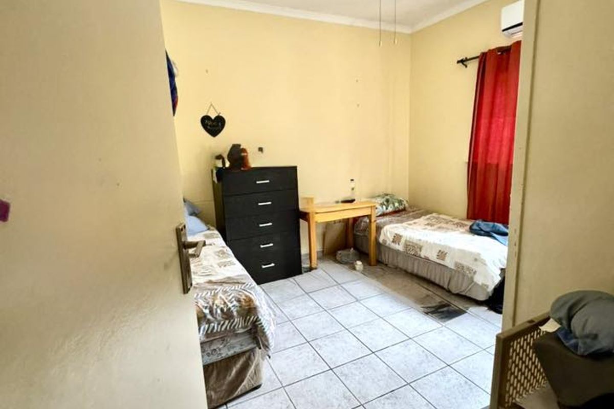 A functional bedroom featuring tiled flooring, a ceiling fan, and wall-mounted air conditioning unit.