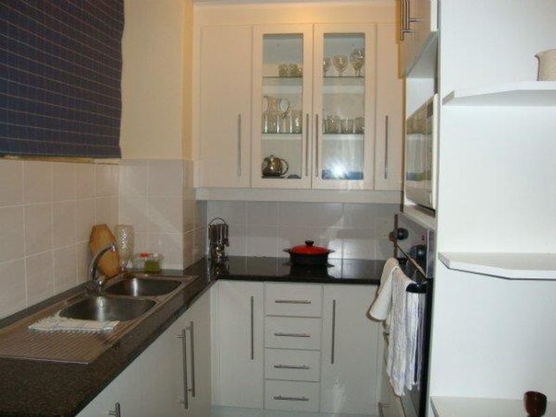 Compact kitchen featuring white cabinetry, granite countertops, a double bowl sink, and a built-in oven with a tiled backsplash.