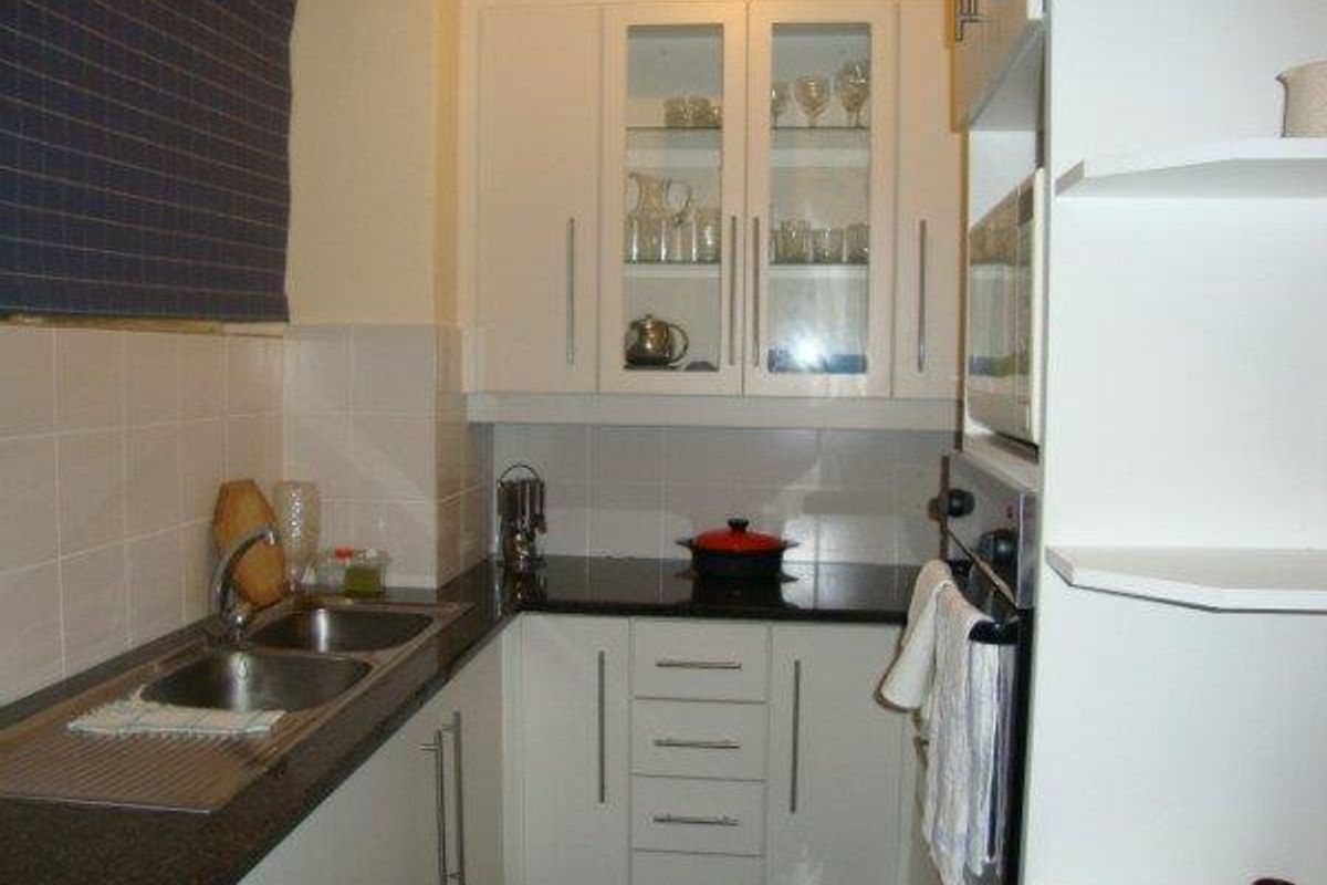 Compact kitchen featuring white cabinetry, granite countertops, a double bowl sink, and a built-in oven with a tiled backsplash.