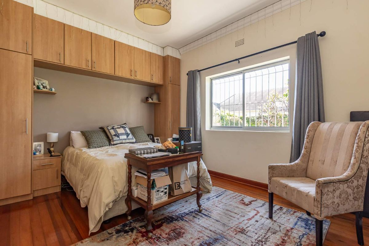A bedroom featuring built-in wooden cupboards surrounding the bed area, hardwood flooring, and a window with security bars.