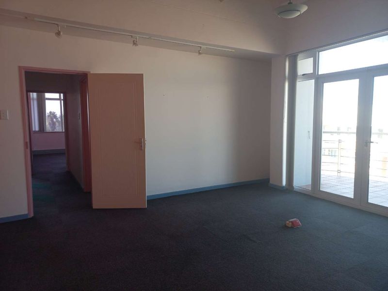 A spacious, empty office area featuring carpeted flooring, track lighting, and large glass doors providing access to an outdoor balcony.