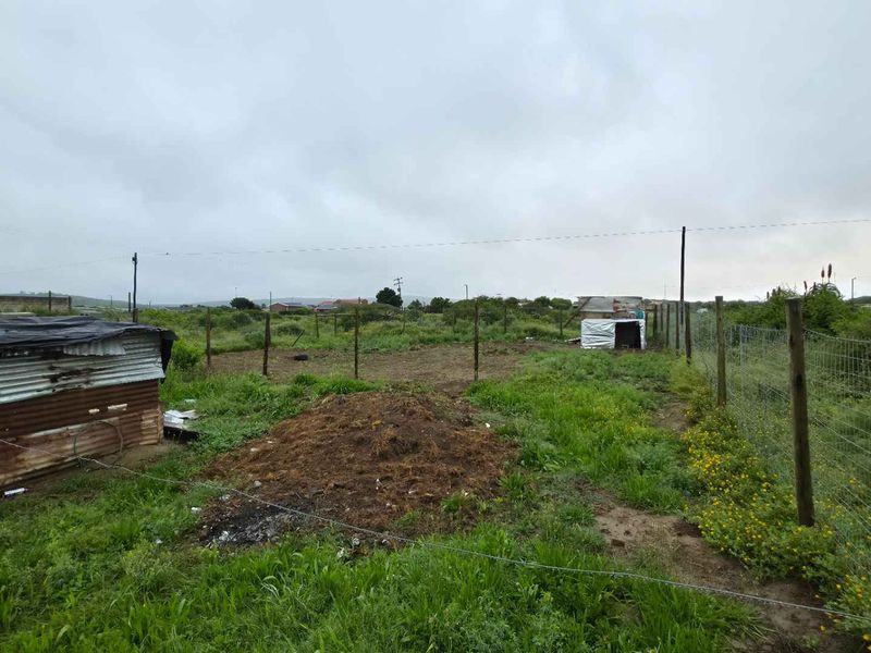 A large, undeveloped plot of land featuring wire mesh perimeter fencing and an existing corrugated metal structure.