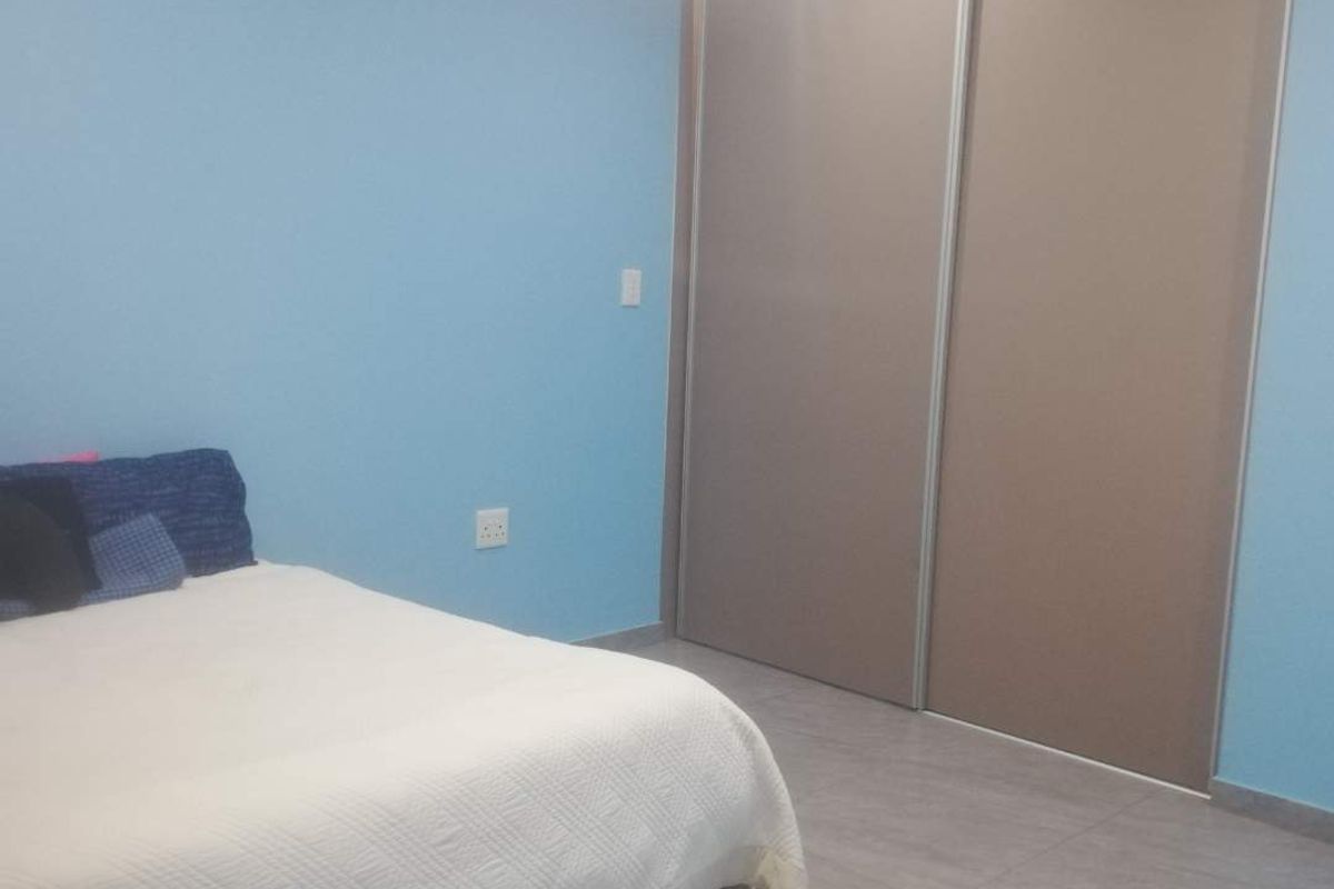 A bedroom featuring light blue walls, large built-in sliding door cupboards, and neutral floor tiling.