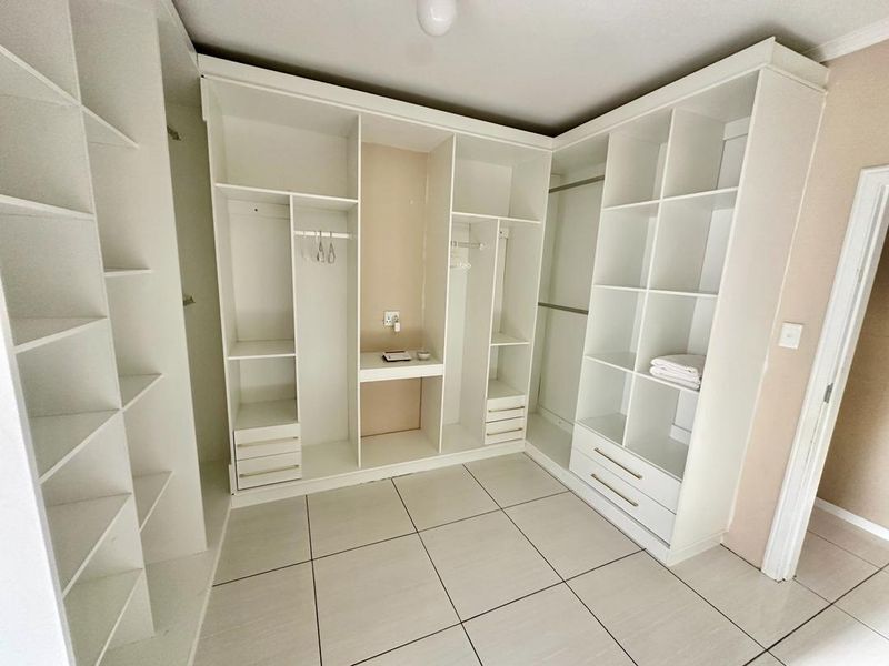 A spacious walk-in closet or dressing area featuring extensive white built-in cabinetry, shelving, and drawers with modern tiled flooring.