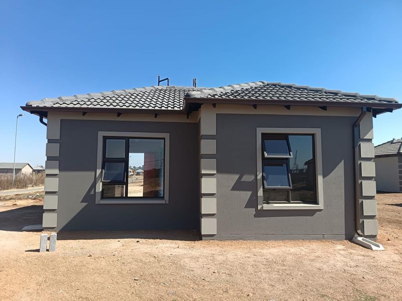 Rear view of a modern single-story house featuring a tiled roof, dark grey plastered walls with contrasting quoins, and aluminium window frames.
