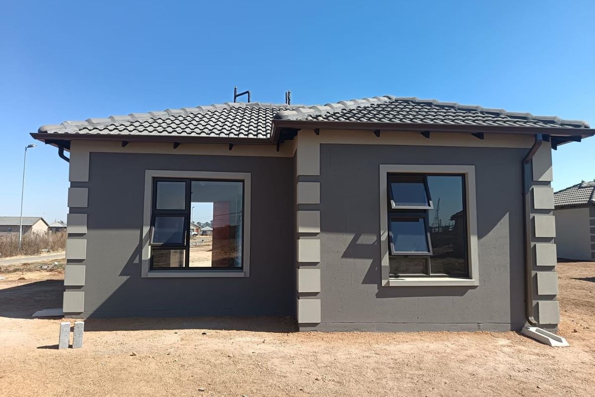 Rear view of a modern single-story house featuring a tiled roof, dark grey plastered walls with contrasting quoins, and aluminium window frames.