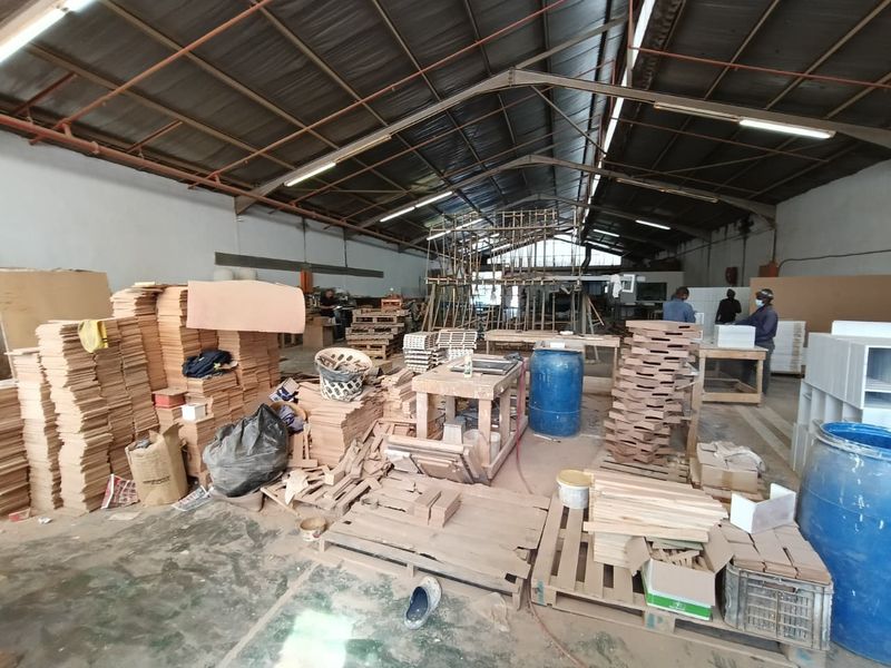 Spacious industrial workshop area featuring high ceilings with exposed steel trusses, fluorescent lighting, and durable concrete flooring, suitable for manufacturing or storage operations.