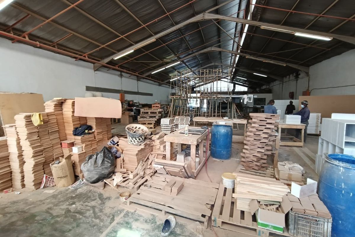 Spacious industrial workshop area featuring high ceilings with exposed steel trusses, fluorescent lighting, and durable concrete flooring, suitable for manufacturing or storage operations.