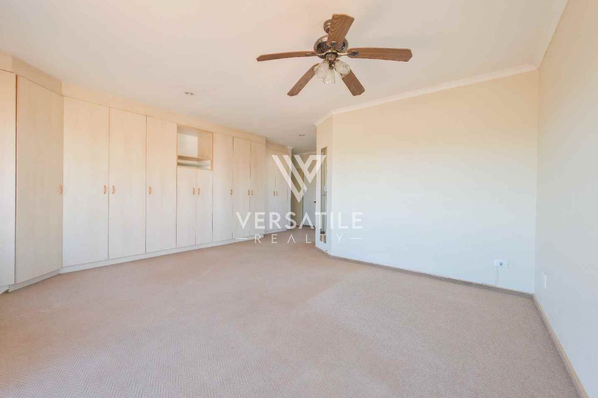 A spacious bedroom featuring extensive built-in cabinetry, neutral carpeting, and a ceiling fan, offering a clean and functional living space.