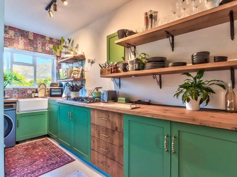A charming kitchen featuring vibrant green cabinetry, natural wooden countertops, open shelving, and a classic farmhouse sink with a decorative tiled backsplash.