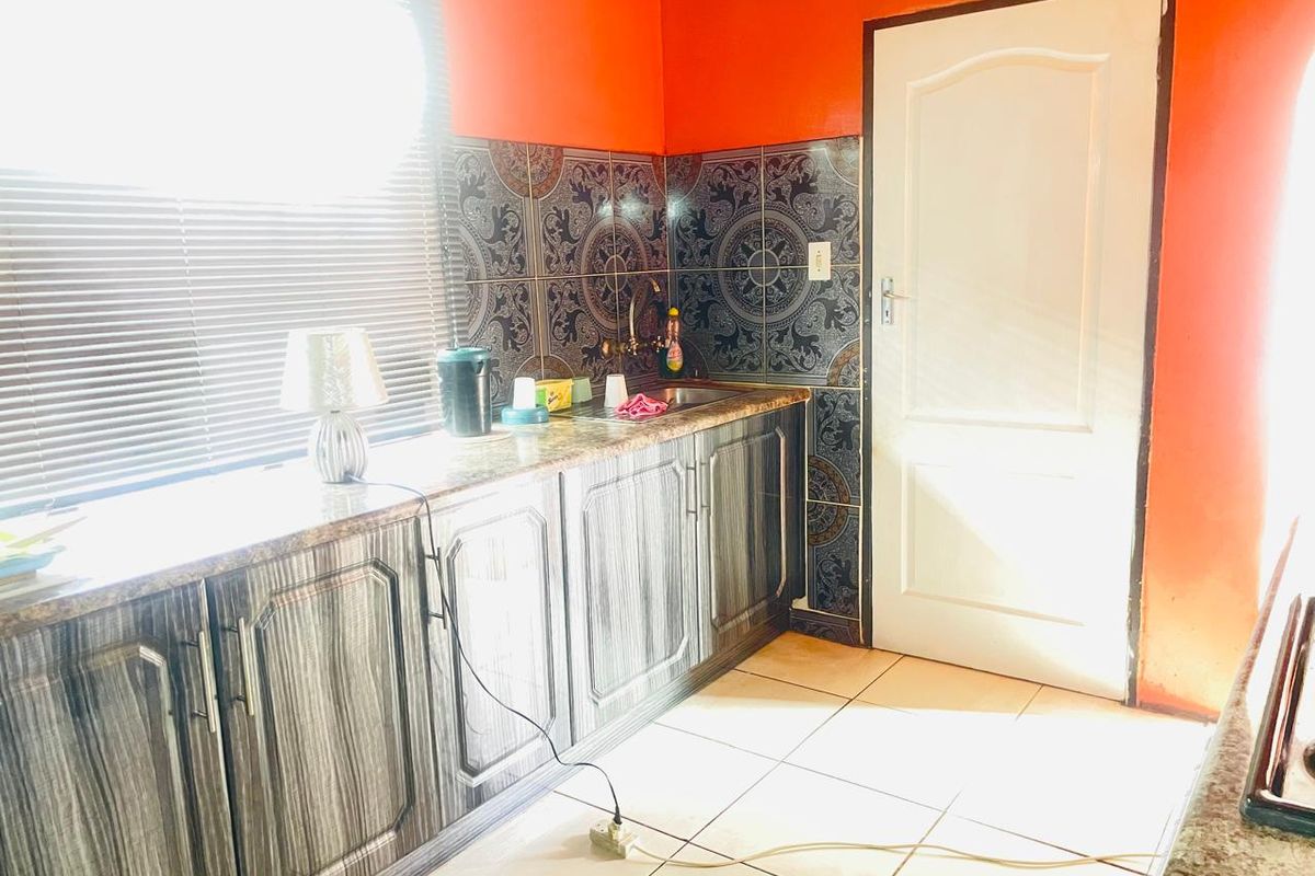 A functional kitchen area featuring wood-grain cabinetry, granite-look countertops, decorative tiled splashbacks, and tiled flooring.