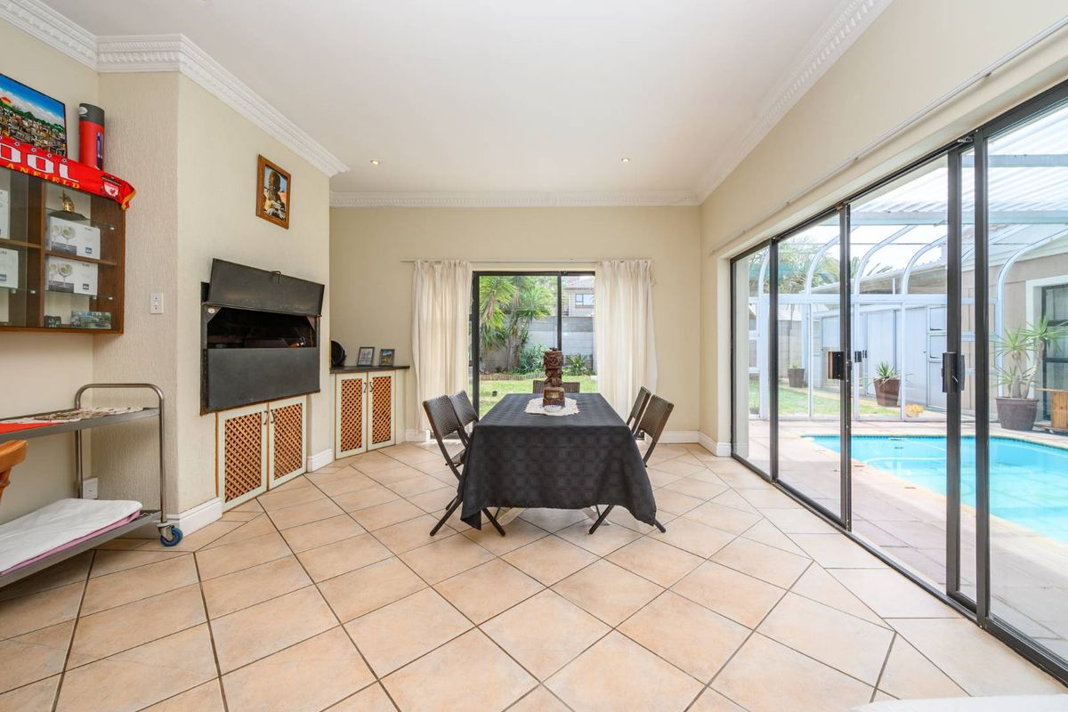 Spacious living area featuring tiled flooring, a built-in braai, and large sliding glass doors providing direct access to the pool area.