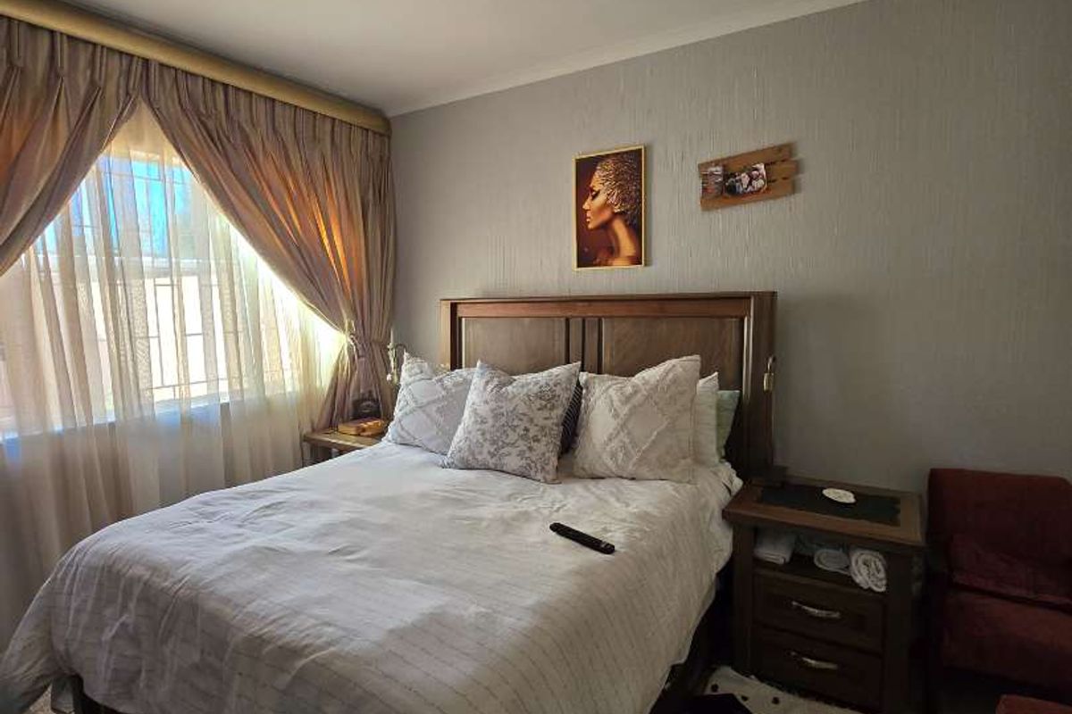 A cozy bedroom featuring neutral wall finishes, a flush mount ceiling light, and a window fitted with security bars.