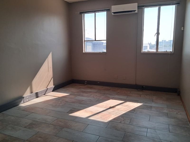 A bright, empty office space featuring tiled flooring, wall-mounted air conditioning, and integrated electrical trunking along the baseboards.