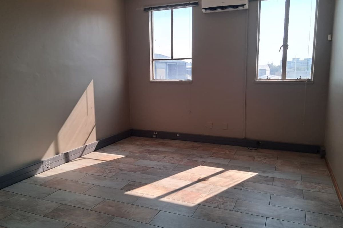 A bright, empty office space featuring tiled flooring, wall-mounted air conditioning, and integrated electrical trunking along the baseboards.