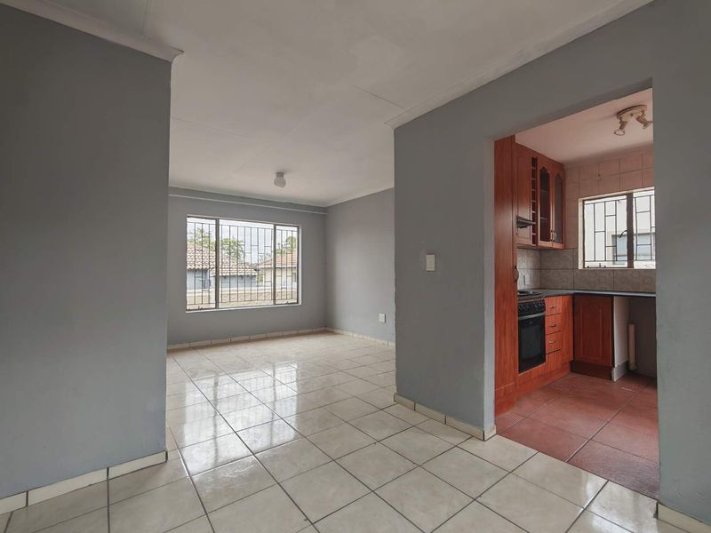 Open plan living area featuring tiled floors and a connected kitchen with built-in cabinetry, oven, and hob, offering a functional layout.