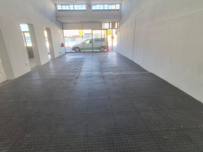 An empty, open-plan commercial space featuring rubber flooring, ceiling fans, and a large glass storefront window, suitable for various business uses.