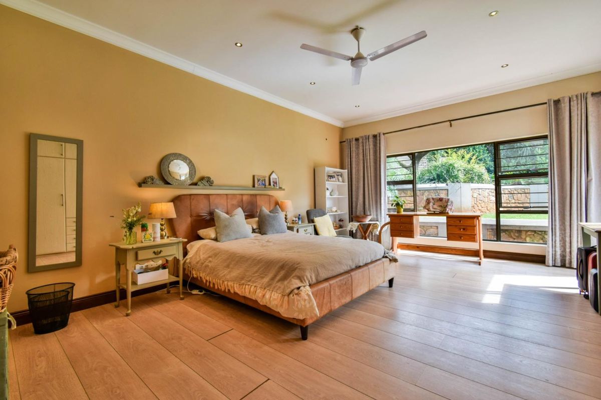 Spacious bedroom featuring light wood-look flooring, recessed ceiling lighting, a modern ceiling fan, and large windows providing natural light and garden views.