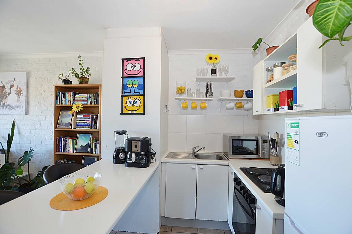 Compact kitchen featuring white cabinetry, a breakfast bar, built-in oven, electric hob, and tiled backsplash, offering a functional and efficient cooking space.