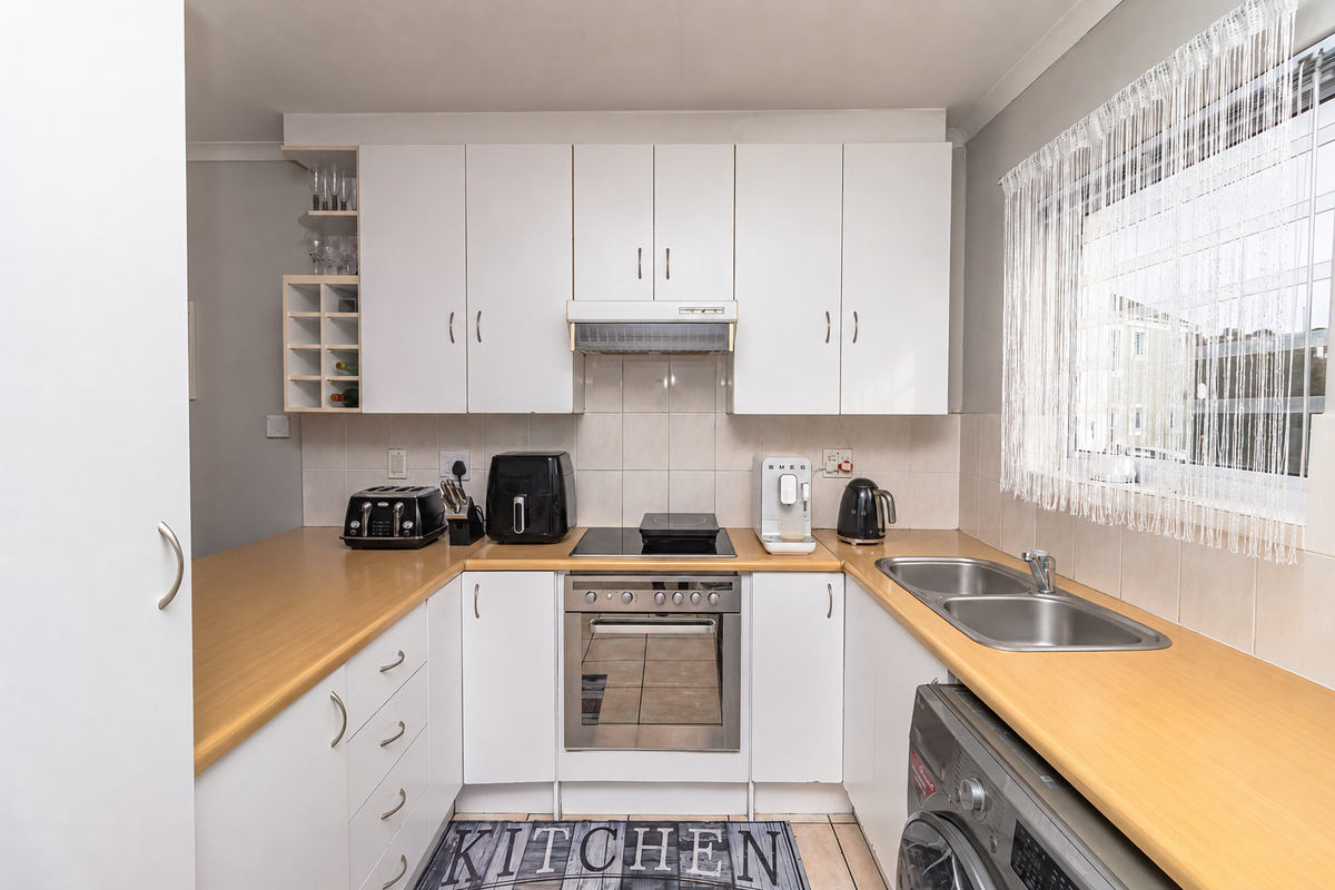 A functional kitchen featuring white cabinetry, laminate countertops, a built-in oven with hob, and a stainless steel sink with tiled backsplash.