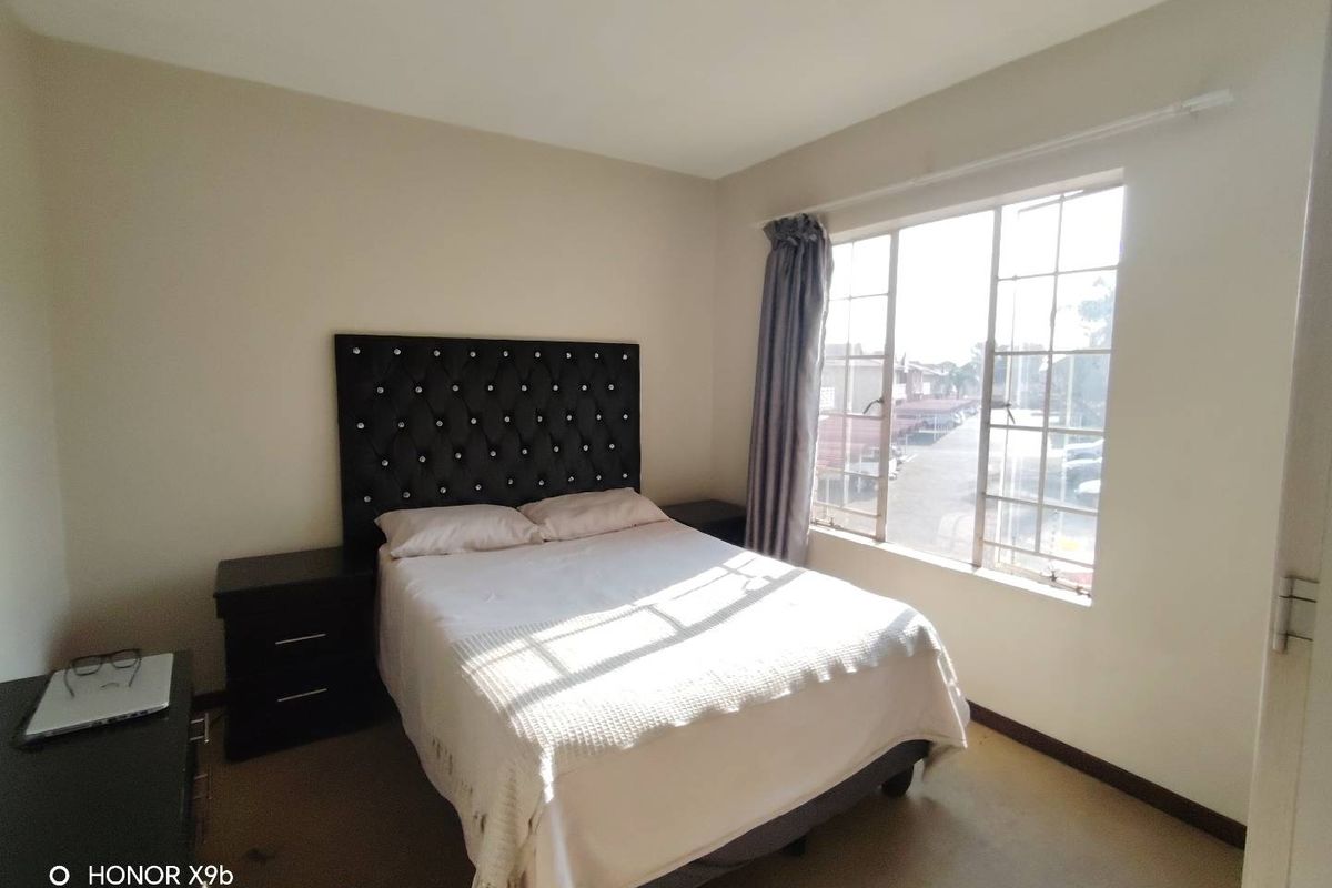 A functional bedroom featuring a large window with metal frames, providing natural light and a view of the surrounding area.