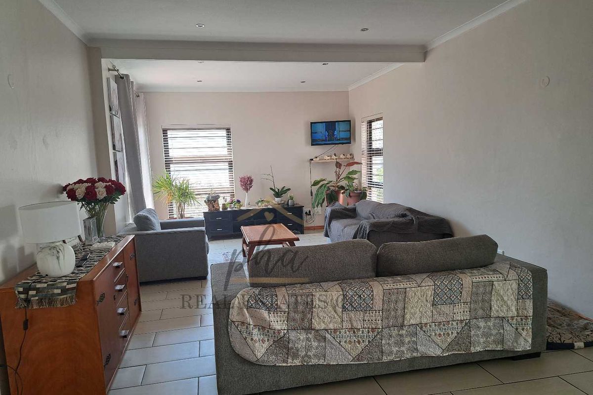 A spacious living room featuring neutral tiled flooring, recessed ceiling lighting, and large windows that provide ample natural light.