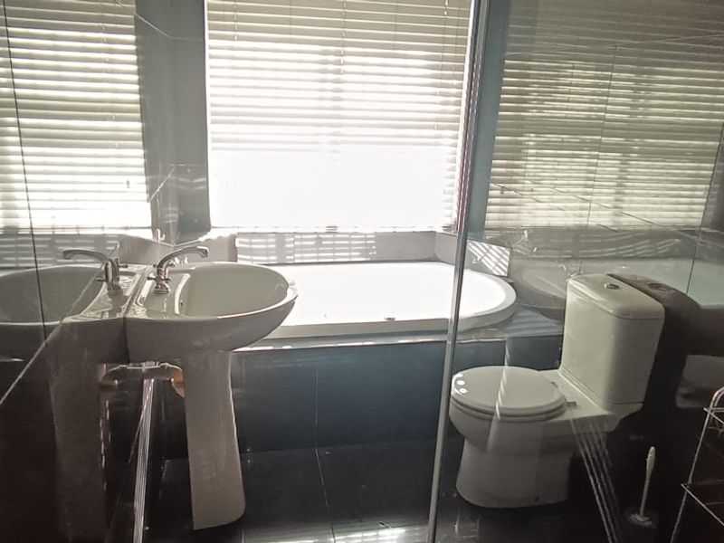 A functional bathroom featuring a pedestal basin, a built-in bathtub, and a toilet, finished with dark wall and floor tiles.