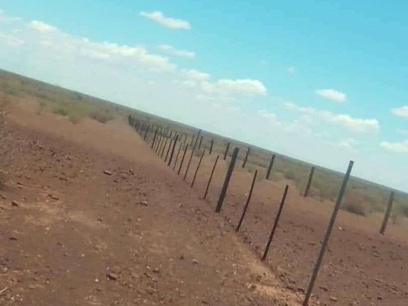 A wide-angle view of the expansive farm landscape featuring a long stretch of wire fencing and fence posts across the arid terrain.