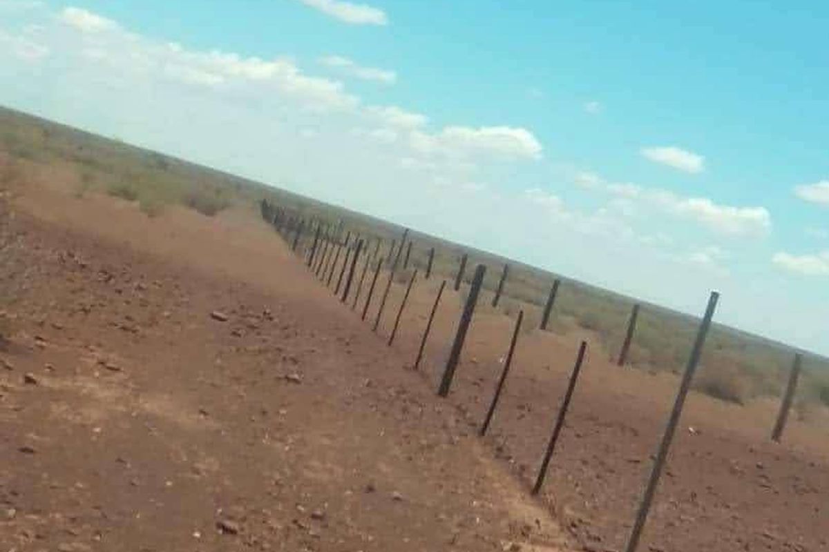 A wide-angle view of the expansive farm landscape featuring a long stretch of wire fencing and fence posts across the arid terrain.