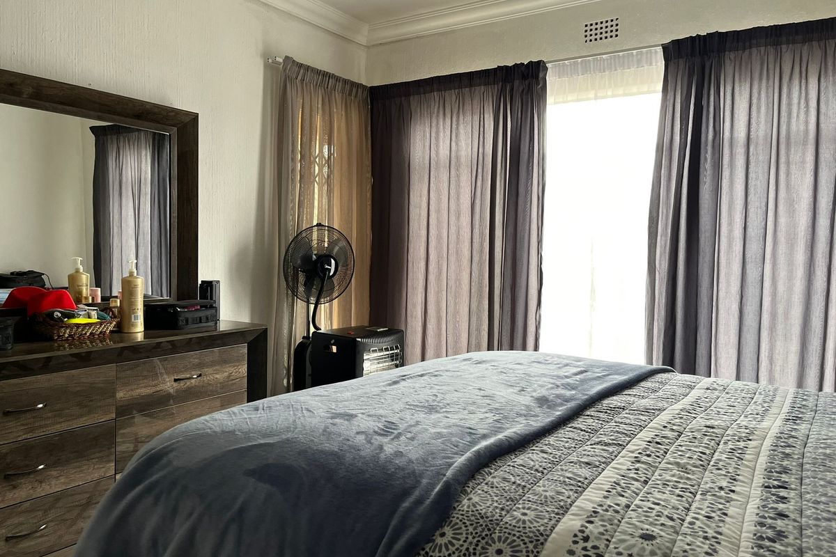 A bedroom featuring neutral walls, decorative cornice detailing, and a ventilation grille, with natural light entering through large window curtains.