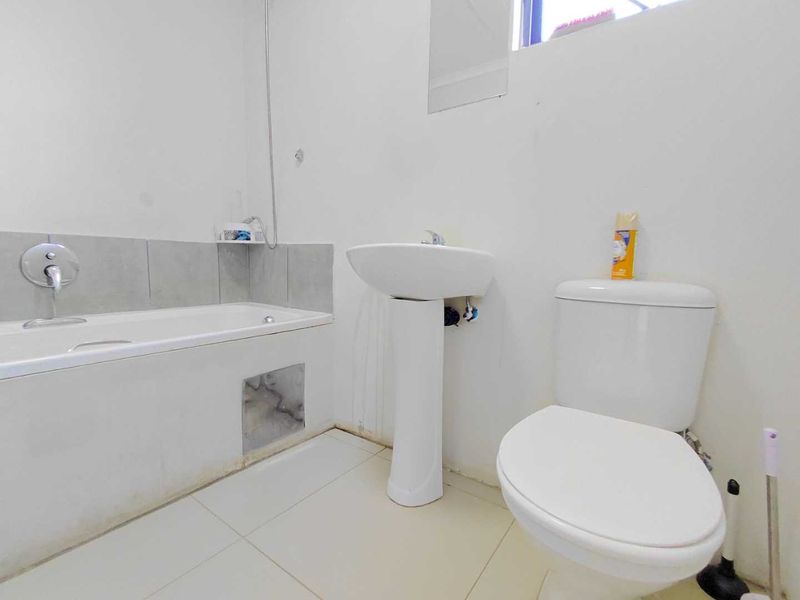 A functional bathroom featuring a pedestal basin, standard toilet, and a bathtub with tiled splashback, requiring minor maintenance and cosmetic updates.