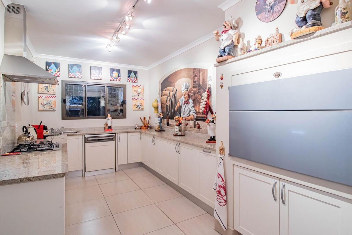 A well-maintained kitchen featuring granite countertops, integrated appliances, gas cooktop, stainless steel extractor fan, and ample built-in cabinetry with tiled flooring.