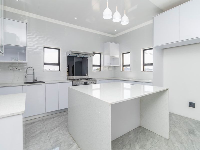 Modern, bright kitchen featuring white cabinetry, a central quartz island, gas stove with extractor, and sleek tiled flooring throughout.