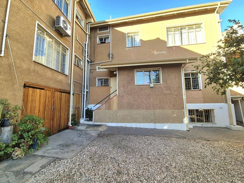 Rear exterior view of the apartment building featuring a gravel courtyard, timber garage doors, and security-fitted windows.